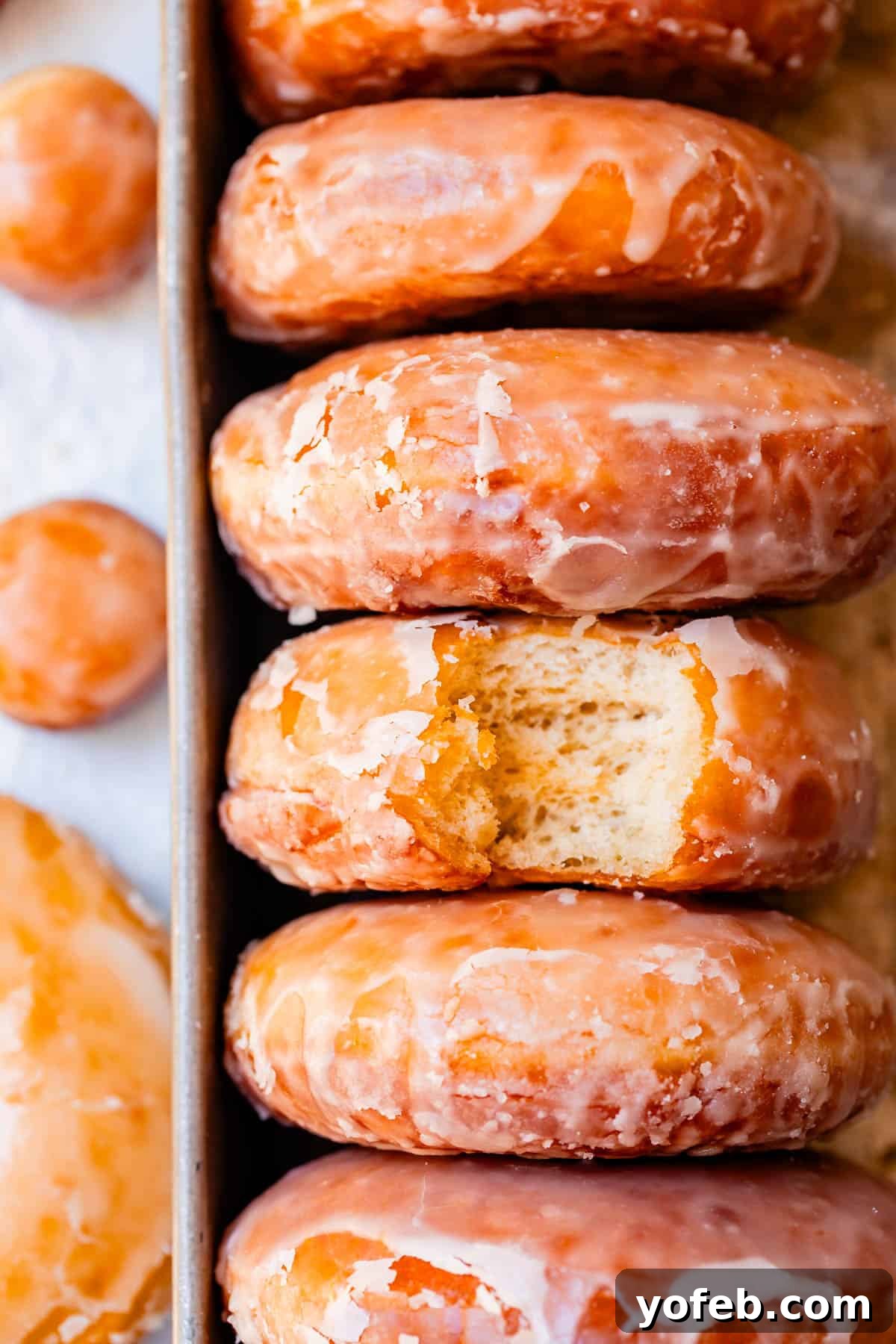 Doughnut Delights from Scratch 39 A tray holding five glazed donuts stacked sideways, with a tempting bite taken out of the middle donut.