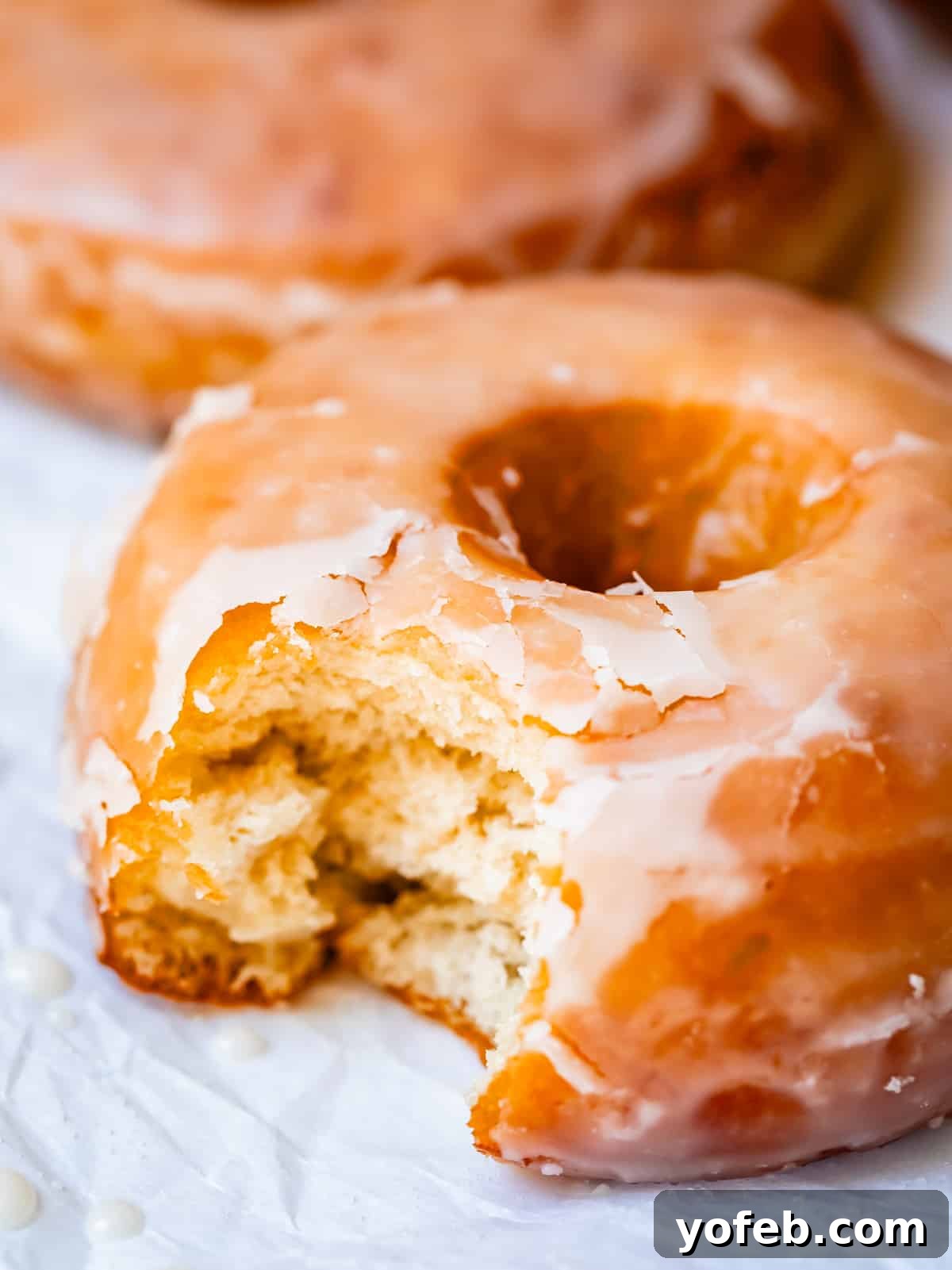 Doughnut Delights from Scratch 40 Close-up of a single homemade donut with a bite taken out of it, sitting on parchment paper, emphasizing its perfect fluffy texture.