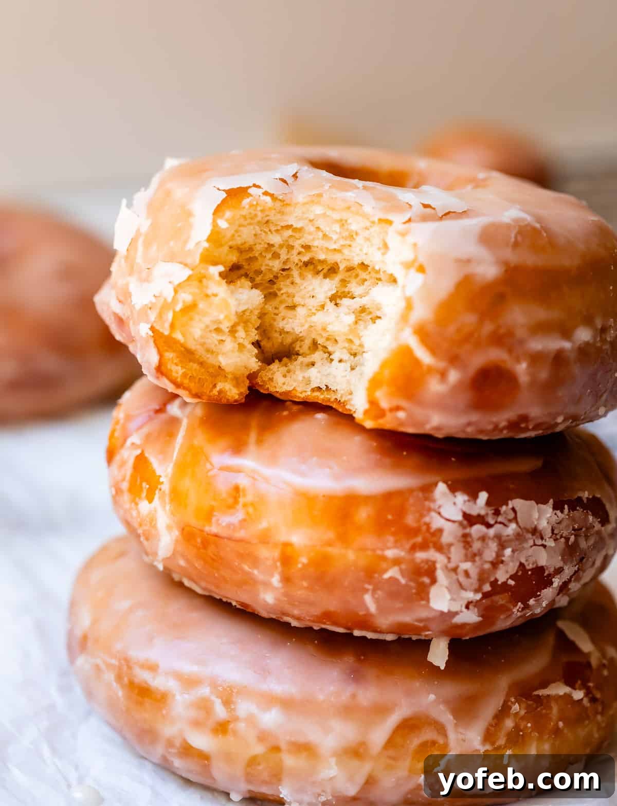 Doughnut Delights from Scratch 9 A stack of three soft yeast donuts on parchment paper, with a delightful bite taken from the top donut.