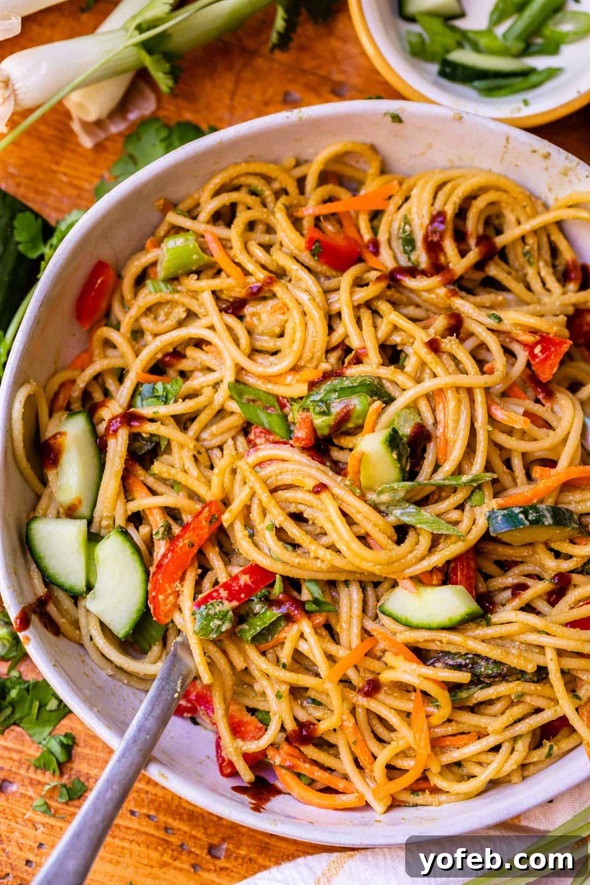 Vibrant Spring Sesame Noodles 2 A ceramic bowl brimming with cold sesame noodles and a mix of vibrant vegetables, ready to be enjoyed.