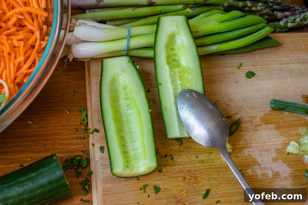 Vibrant Spring Sesame Noodles 13 A spoon scraping the seeds and soft center out of a halved cucumber, preparing it for inclusion in sesame noodles.