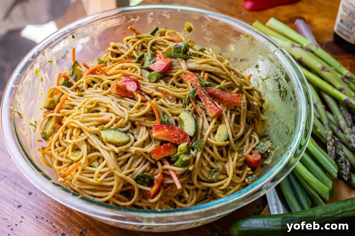 Vibrant Spring Sesame Noodles 16 Noodles mixed thoroughly with the rich sesame sauce and a variety of colorful vegetables in a large glass serving bowl.