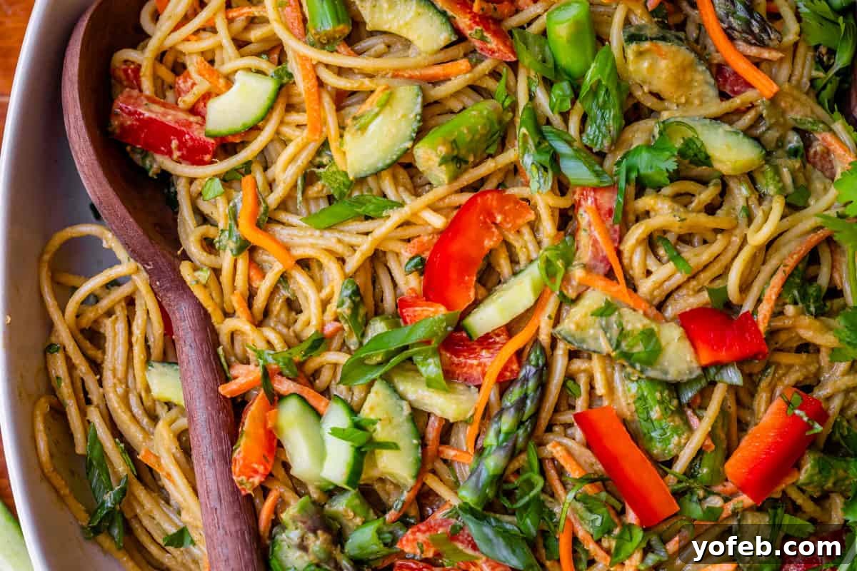 Vibrant Spring Sesame Noodles 17 Close-up of cold sesame noodles artfully arranged in a bowl, featuring crisp red bell pepper, fresh cucumber, and tender asparagus.