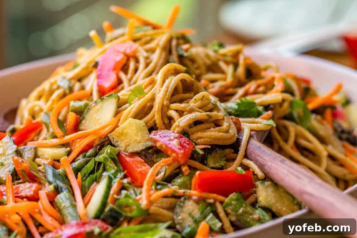 Vibrant Spring Sesame Noodles 19 Side view of cold sesame noodles and fresh vegetables generously topped with sauce, overflowing in a ceramic bowl.