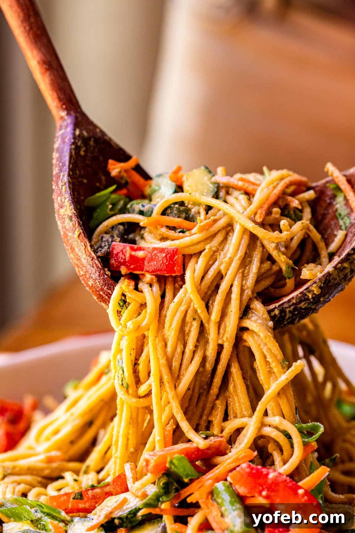 Vibrant Spring Sesame Noodles 3 Two wooden salad spoons lifting a generous portion of sesame peanut noodles and mixed vegetables from a bowl, showcasing their delicious coating.