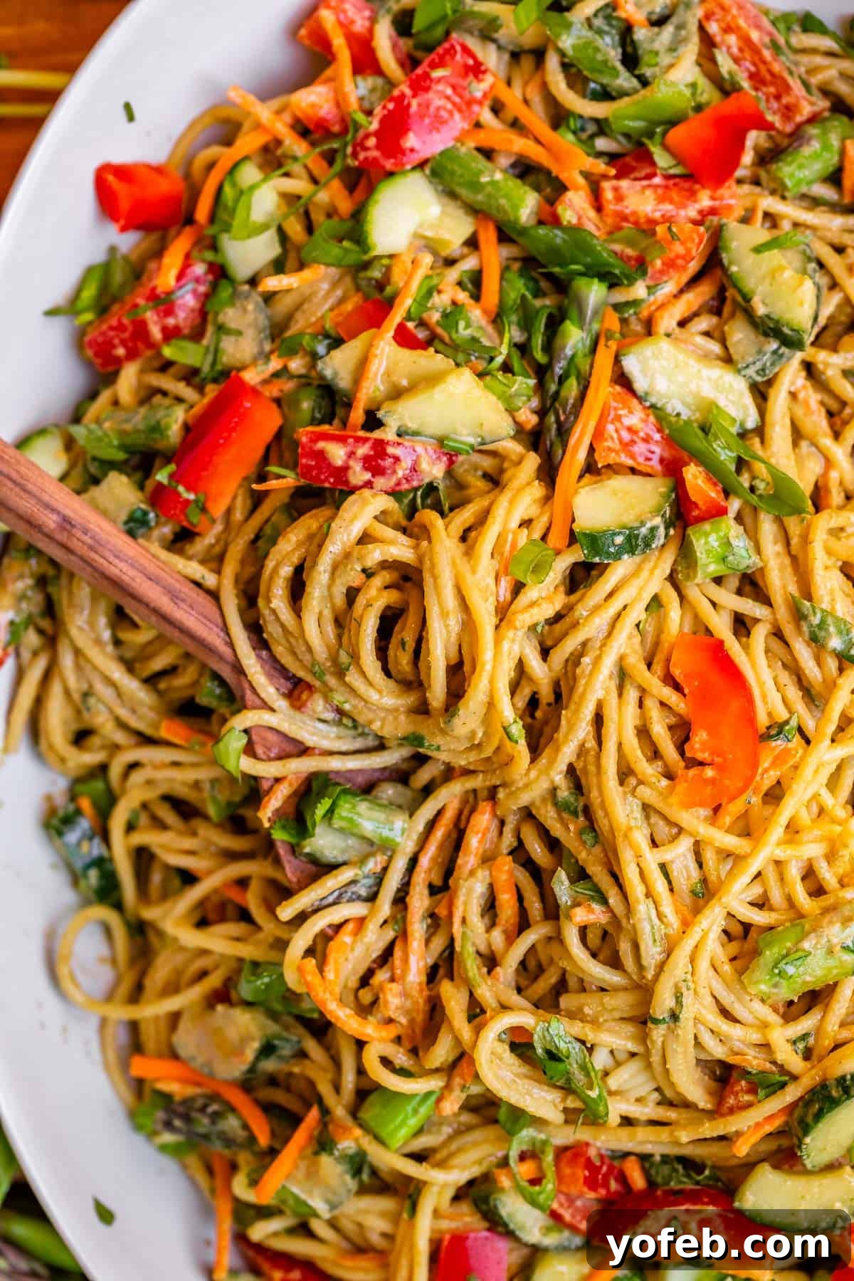 Vibrant Spring Sesame Noodles 20 Top-down shot of a large platter filled with beautifully arranged sesame peanut noodles and mixed vegetables, with a serving spoon ready.