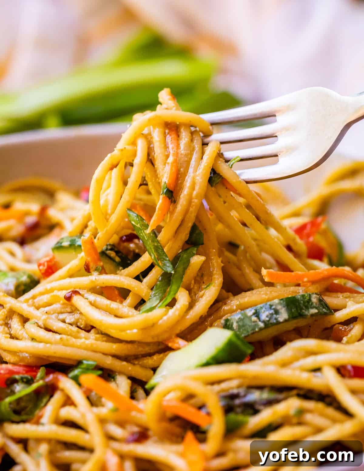 Vibrant Spring Sesame Noodles 4 Close-up shot of thin spaghetti noodles coated in a rich sesame sauce, being lifted by a fork, highlighting their glossy texture.