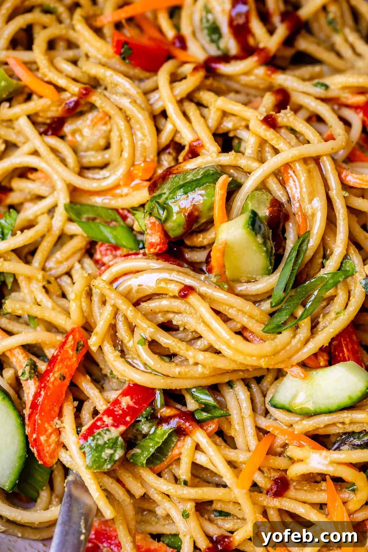 Vibrant Spring Sesame Noodles 5 Close-up of swirled, cold spaghetti noodles generously coated in sesame peanut sauce and mixed with fresh vegetables in a bowl.
