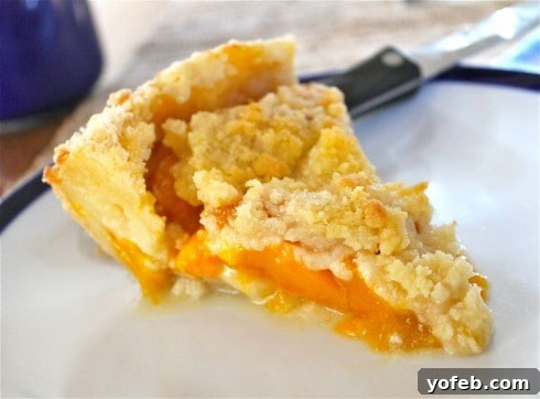 Golden Peach Dream Pie 2 A close-up of a slice of golden peach crumble pie on a white plate, showcasing a perfectly crumbly topping and luscious, juicy peach filling. A serving knife is partially visible in the background, suggesting a recent cut.