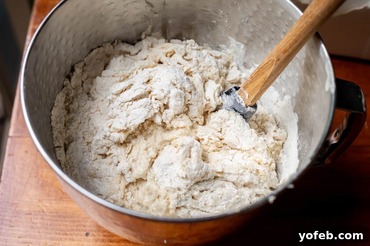 The White Bread Recipe That Ends Your Search 14 A metal mixing bowl with a spoon stirring the flour into the wet mixture, prior to kneading with a dough hook or by hand.