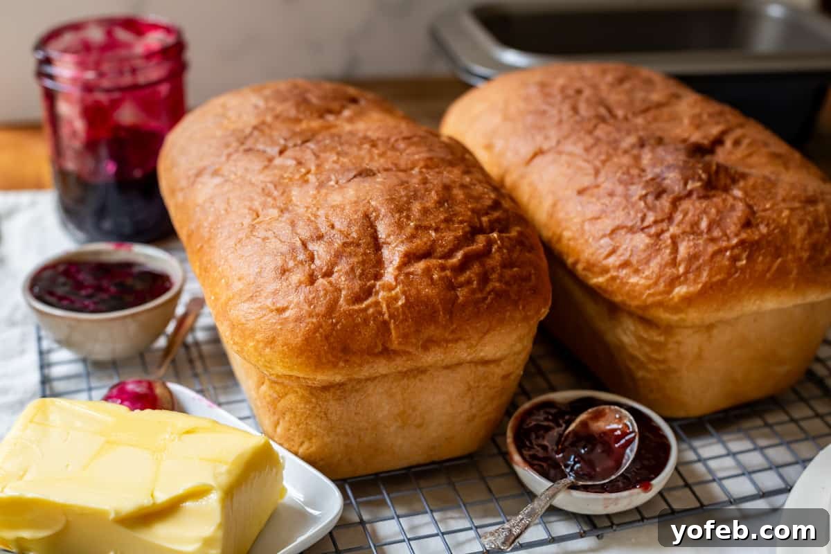 The White Bread Recipe That Ends Your Search 23 Two uncut loaves of fast white bread, fresh from the oven, resting on a cooling rack with small dishes of butter and jam beside them.