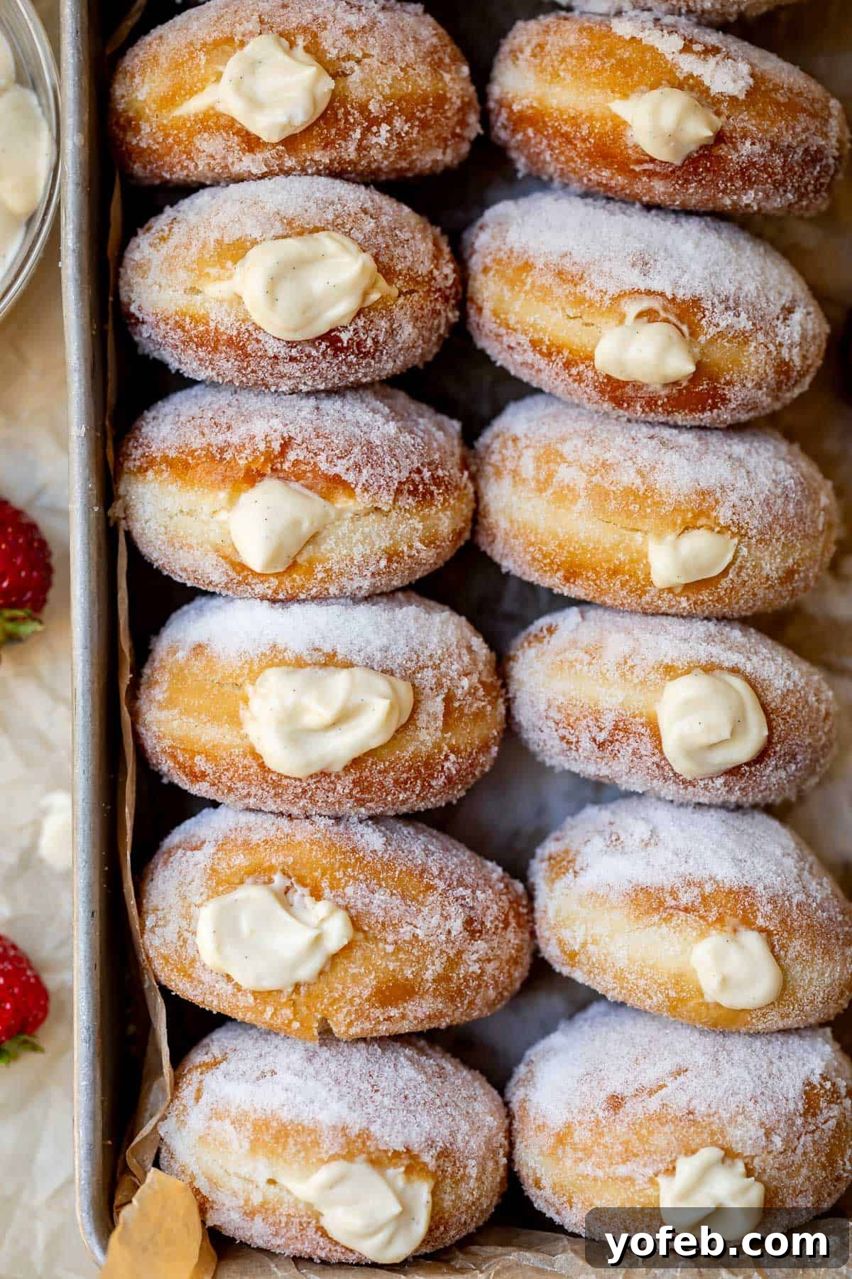 Decadent Bavarian Cream Donuts 3 large metal tray filled with sideways stacked donuts that have been filled with cream.