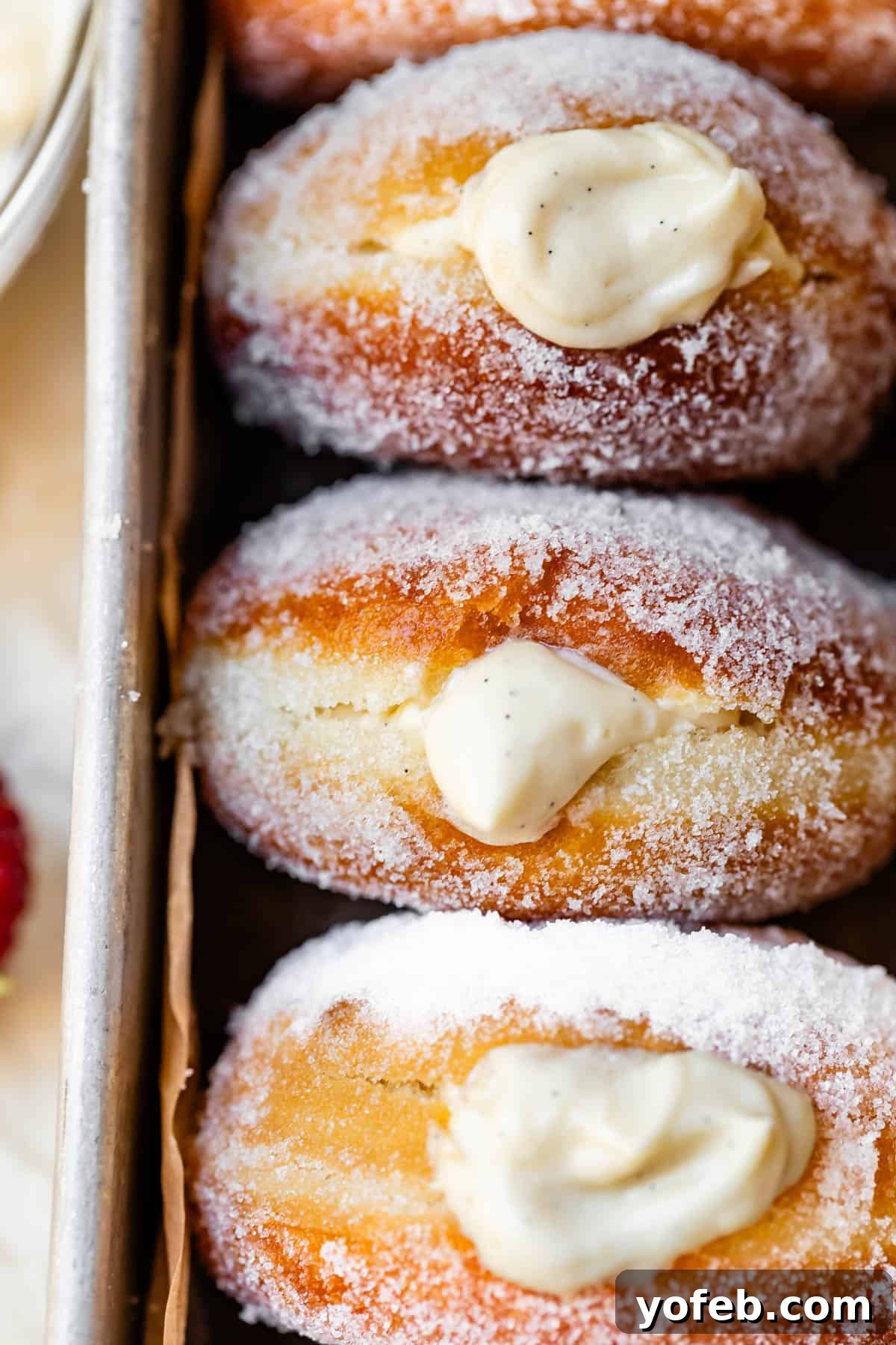 Decadent Bavarian Cream Donuts 28 three sugar rolled donuts puffy with Bavarian cream filling in a metal baking dish.