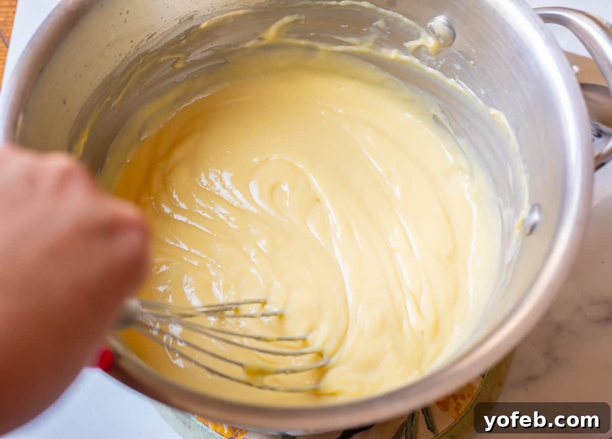 Velvety Crème Pâtissière 13 flat whisk stirring through the just thickened pastry cream still in a metal pot.