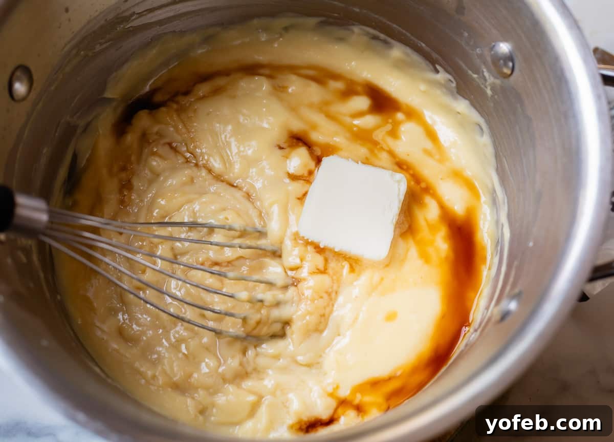 Velvety Crème Pâtissière 14 butter and vanilla being stirred into thickened pastry cream in a silver pot.