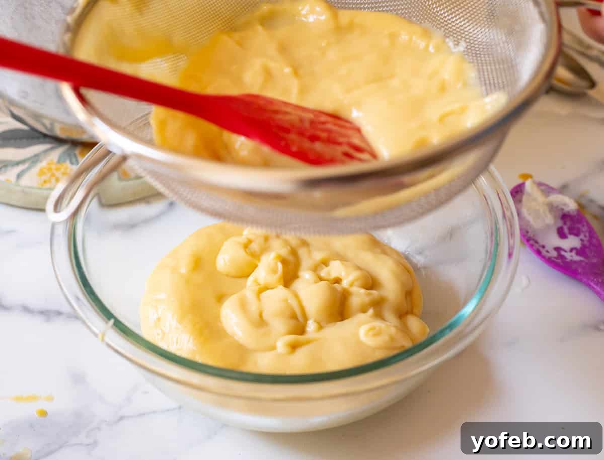 Velvety Crème Pâtissière 15 pushing finished pastry cream through a sieve into a glass bowl to make it extra creamy.