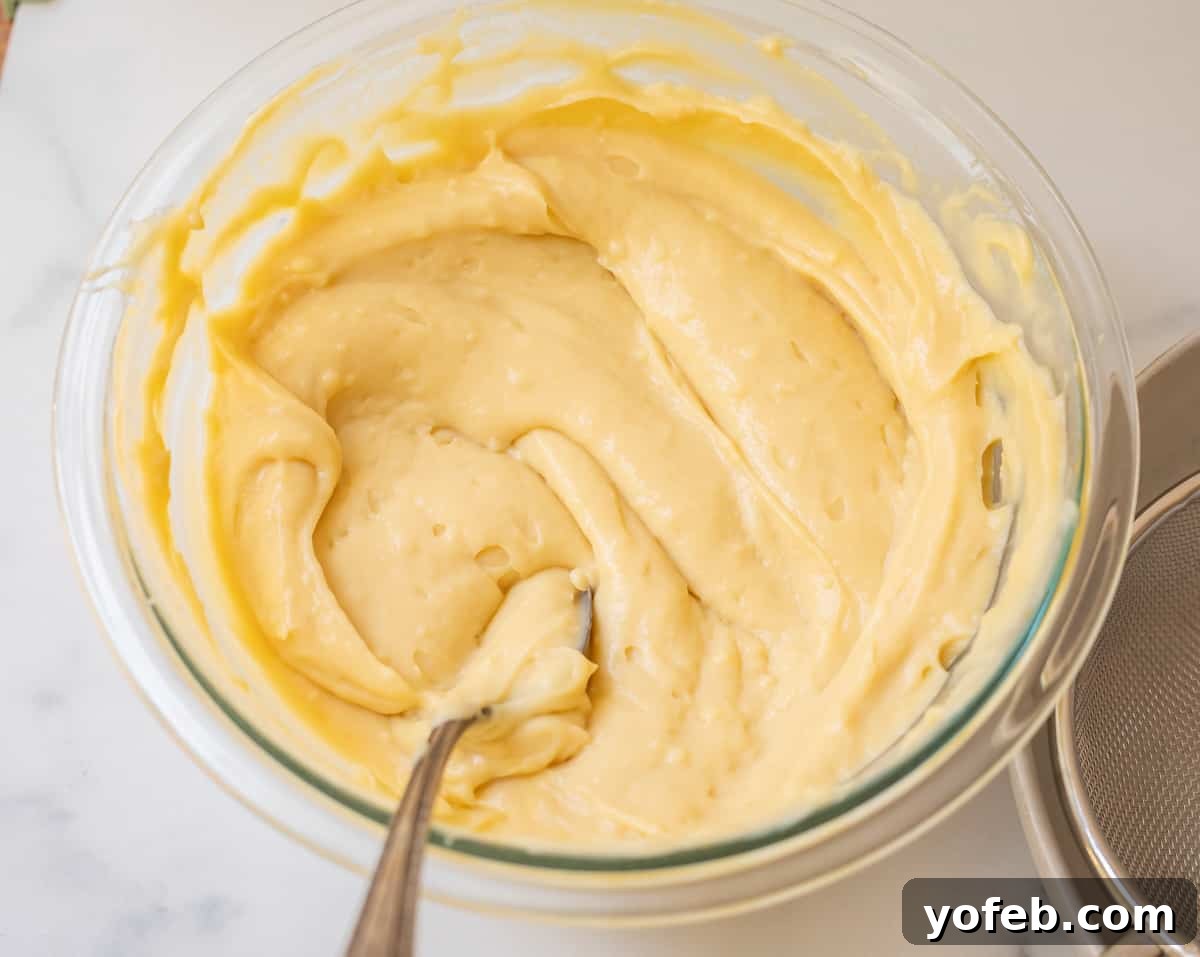 Velvety Crème Pâtissière 17 glass bowl filled with chilled, stirred pastry ream with silver spoon in it.