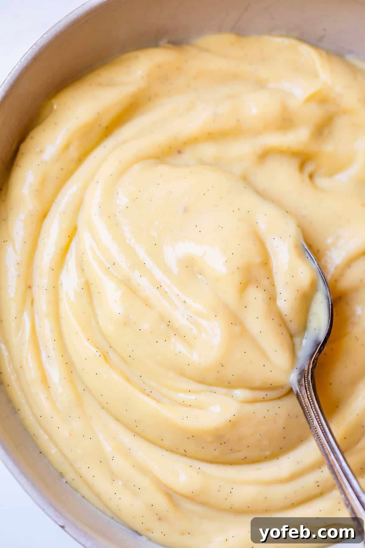 Velvety Crème Pâtissière 21 a silver spoon stirring homemade vanilla pastry cream in a bowl.