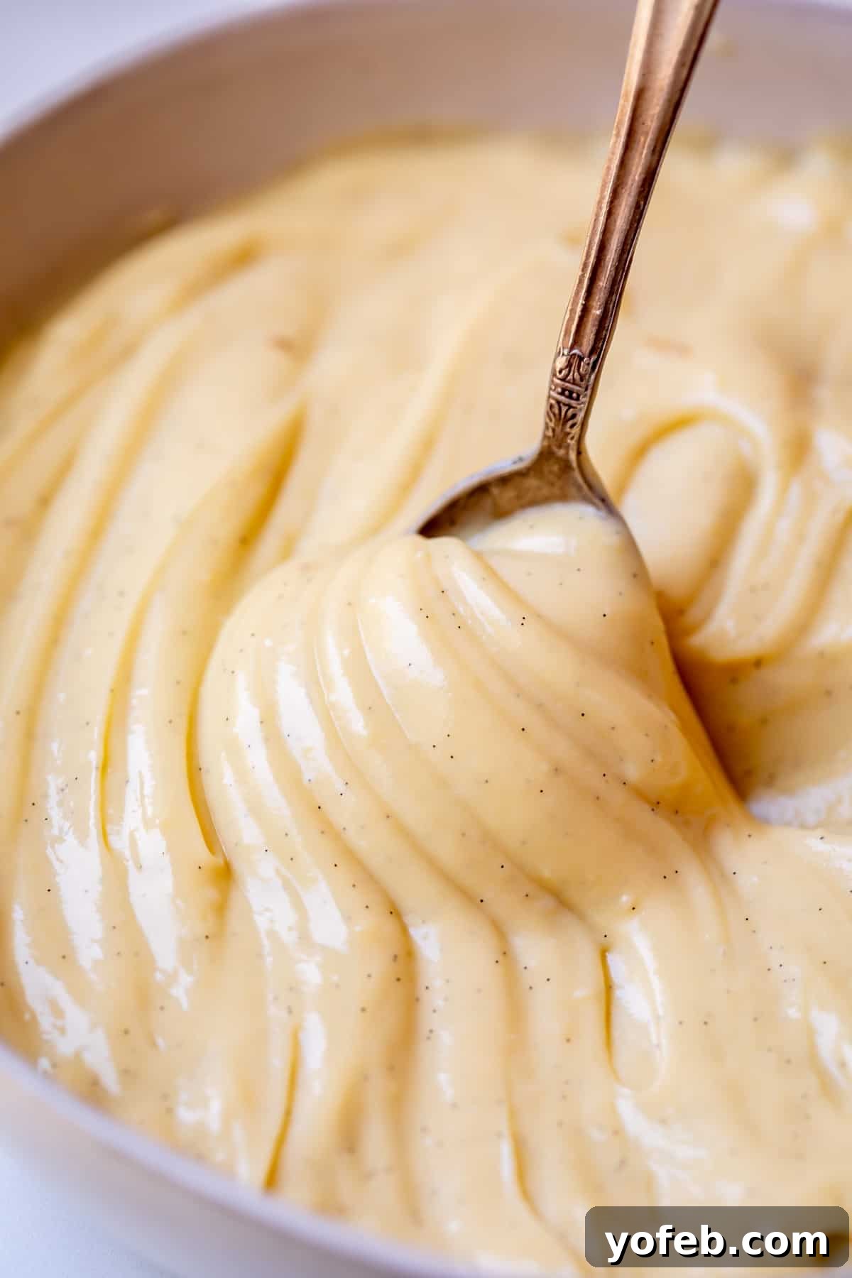 Velvety Crème Pâtissière 4 spoon lifting up as if to pour out pastry cream, but the cream is thick and sticks to the spoon.
