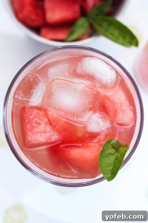 Watermelon Lemon Burst 5 Close-up overhead shot of a single glass of watermelon lemonade, filled with ice and garnished with a fresh basil leaf, showcasing its refreshing allure.