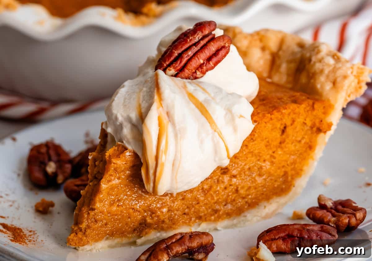 Golden Sweet Potato Pie Crowned with Salted Caramel Cream 30 side view of a tall slice of sweet potato pie with salted caramel whipped cream and a pecan on top.
