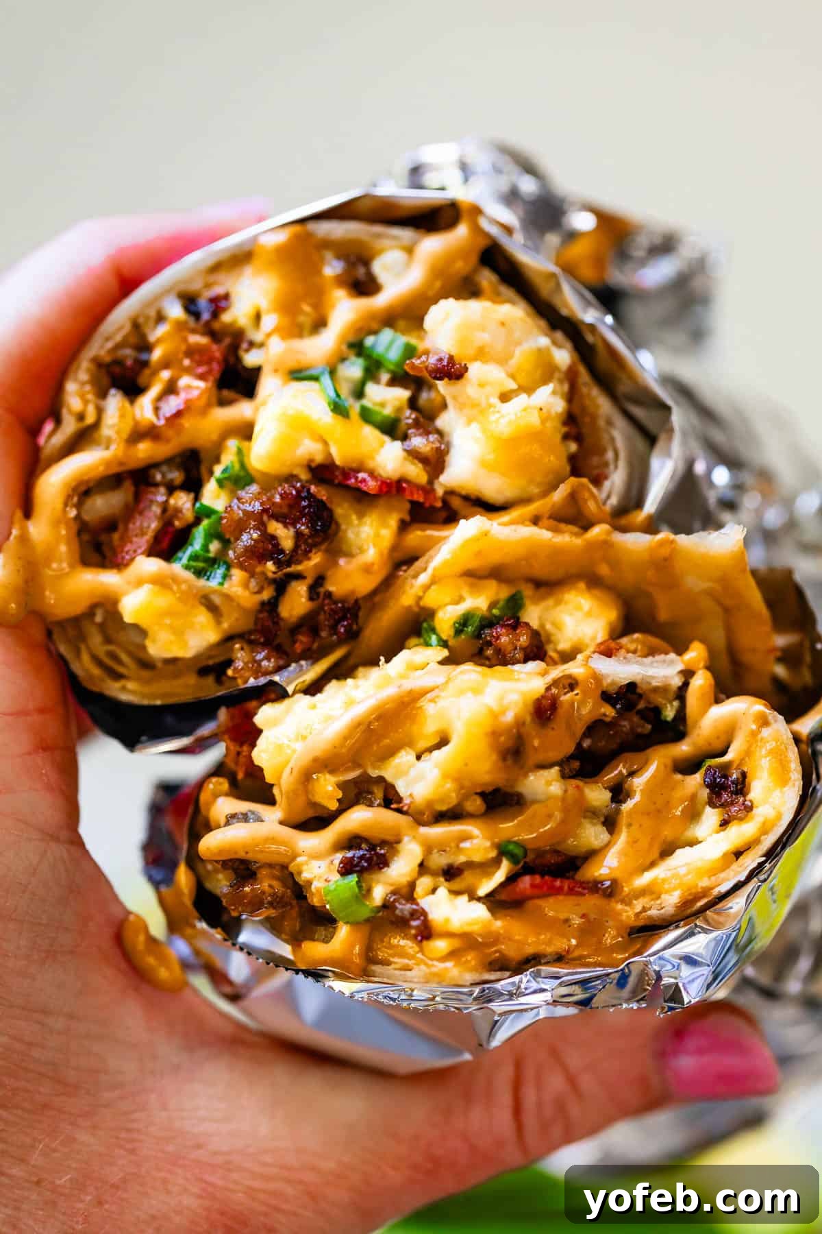 The Ultimate Make Ahead Breakfast Burrito Recipe 25 Two breakfast burrito wrapped in foil with sauce on top with bites taken out.