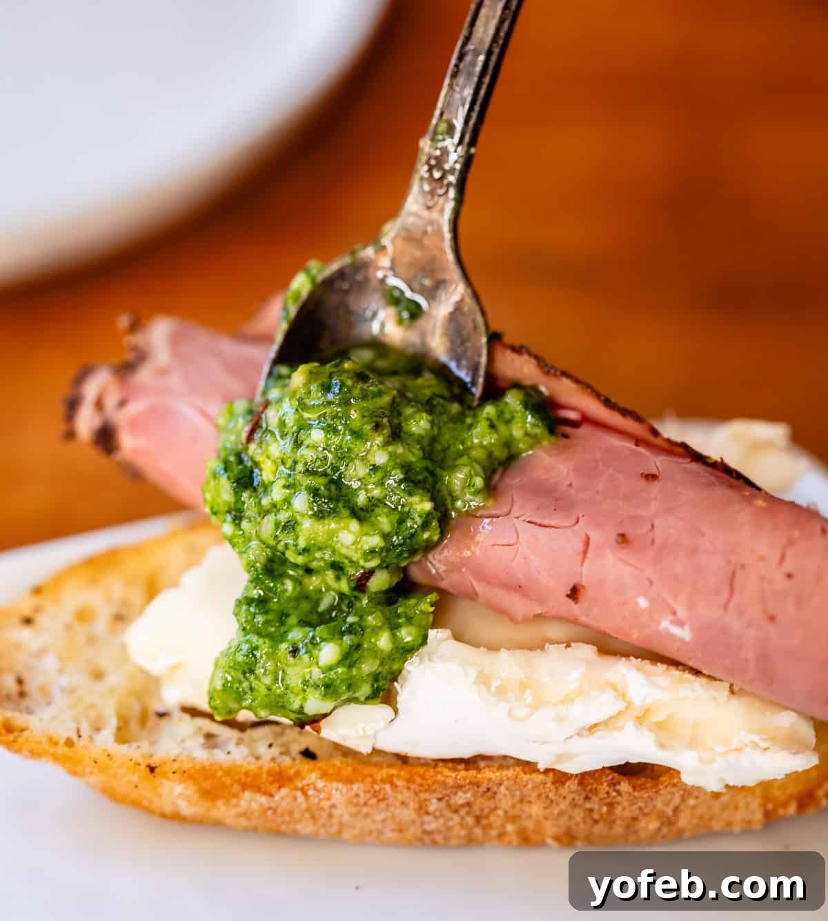 Crafting the Perfect Charcuterie Board 18 Arranging a bite of triple-cream cheese, deli-cut roast beef, homemade pesto, on a slice of baguette close up.