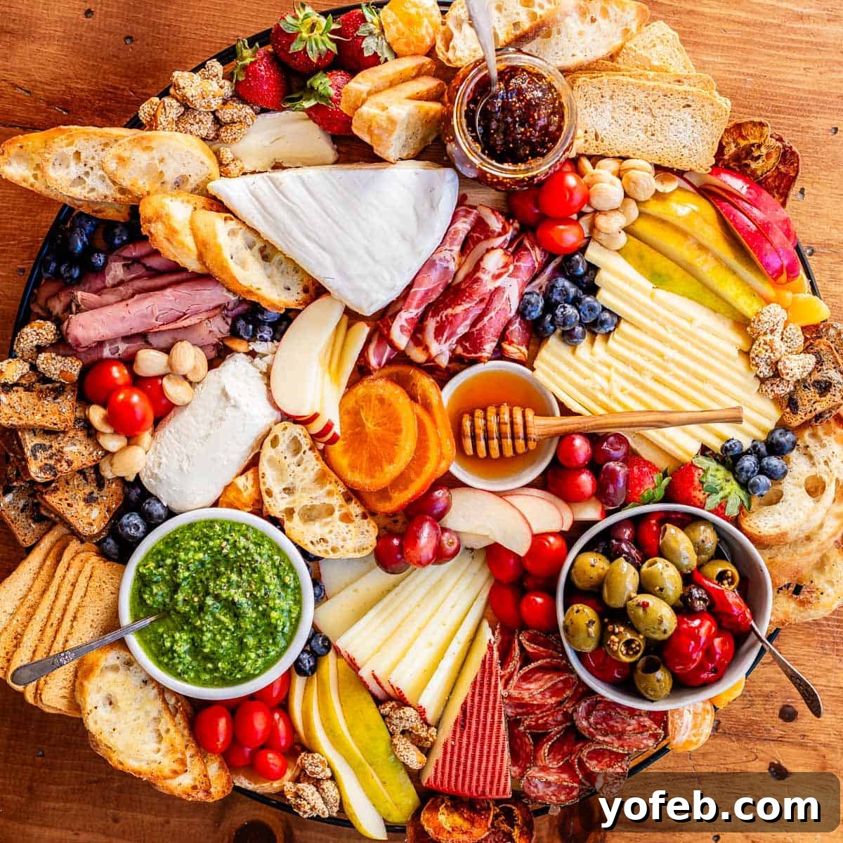Crafting the Perfect Charcuterie Board 19 overhead shot of a round charcuterie board with brie, cheddar, oranges, pesto, crackers, bread, etc.