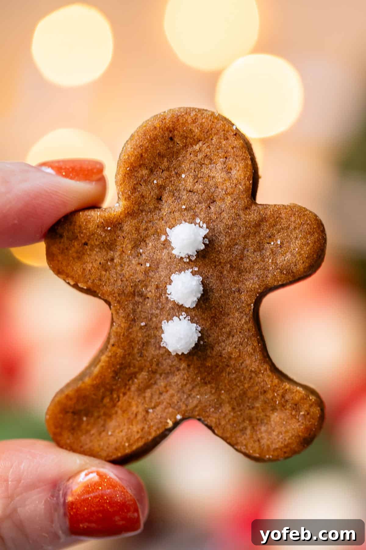 Perfectly Soft Chewy Gingerbread Men That Hold Their Shape 2 Hand holding up a tiny gingerbread man cookie with twinkle lights in the background, showcasing its soft texture and festive appeal.