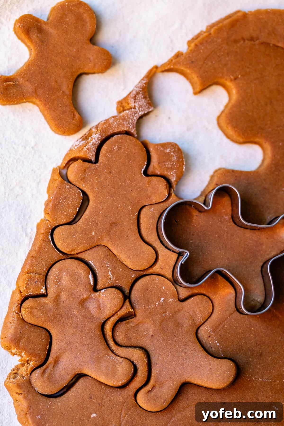 Perfectly Soft Chewy Gingerbread Men That Hold Their Shape 11 A rolled-out section of gingerbread cookie dough, with various cookie cutters poised above it, ready to cut out shapes.