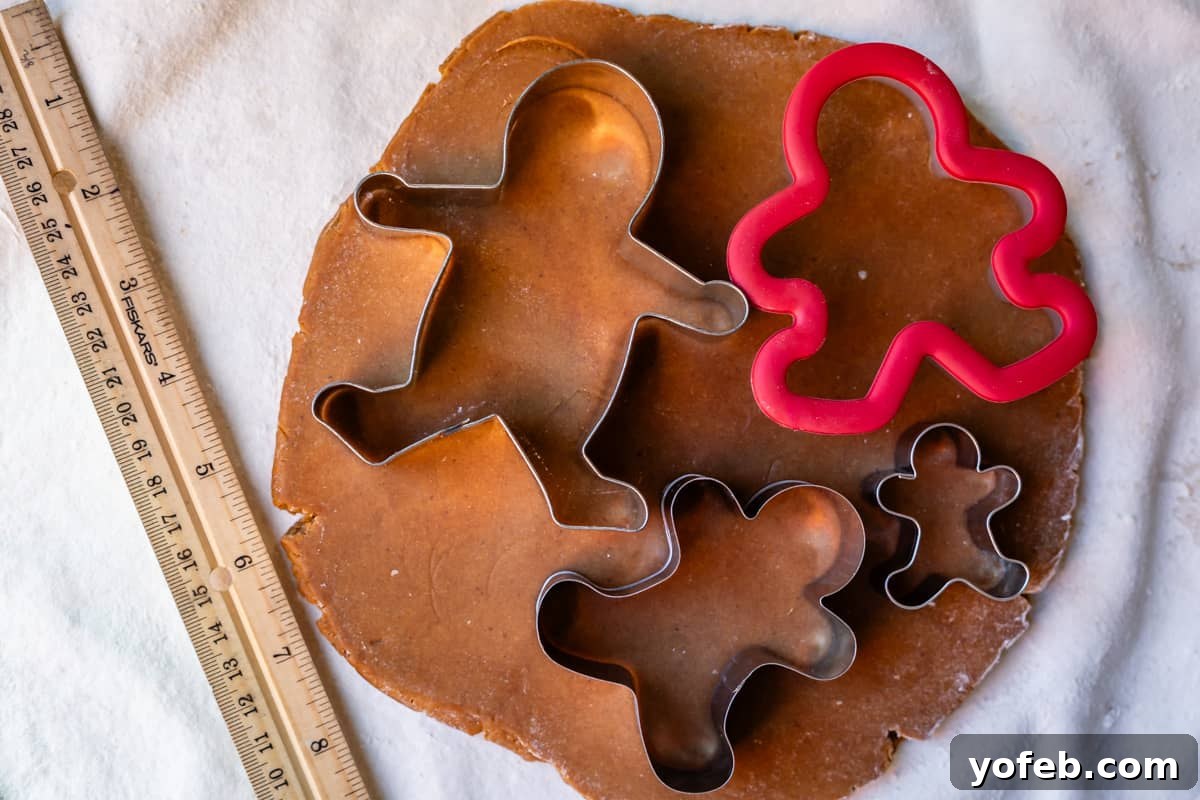 Perfectly Soft Chewy Gingerbread Men That Hold Their Shape 14 Rolled out dough with four different sizes of gingerbread man cookie cutters placed on top, ready for cutting.