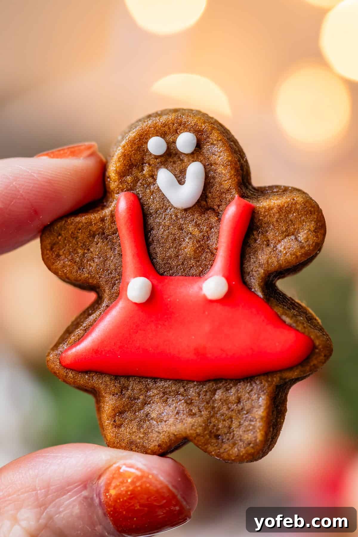 Perfectly Soft Chewy Gingerbread Men That Hold Their Shape 15 A hand holding up a tiny gingerbread cookie adorned with a festive red dress and white icing.