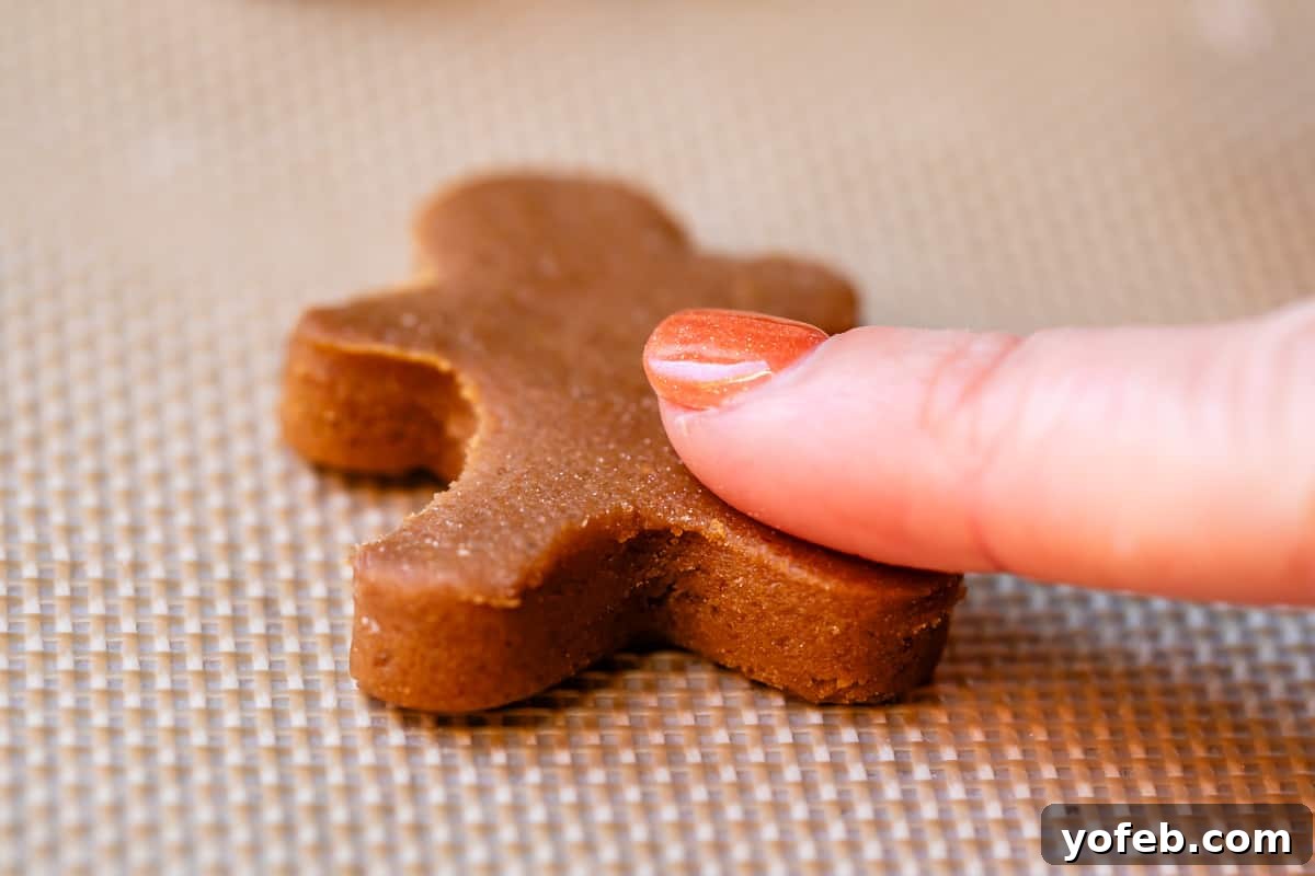 Perfectly Soft Chewy Gingerbread Men That Hold Their Shape 23 A tiny 2-inch cut-out gingerbread man cookie on a Silpat, with a finger gently brushing excess flour from its sides.