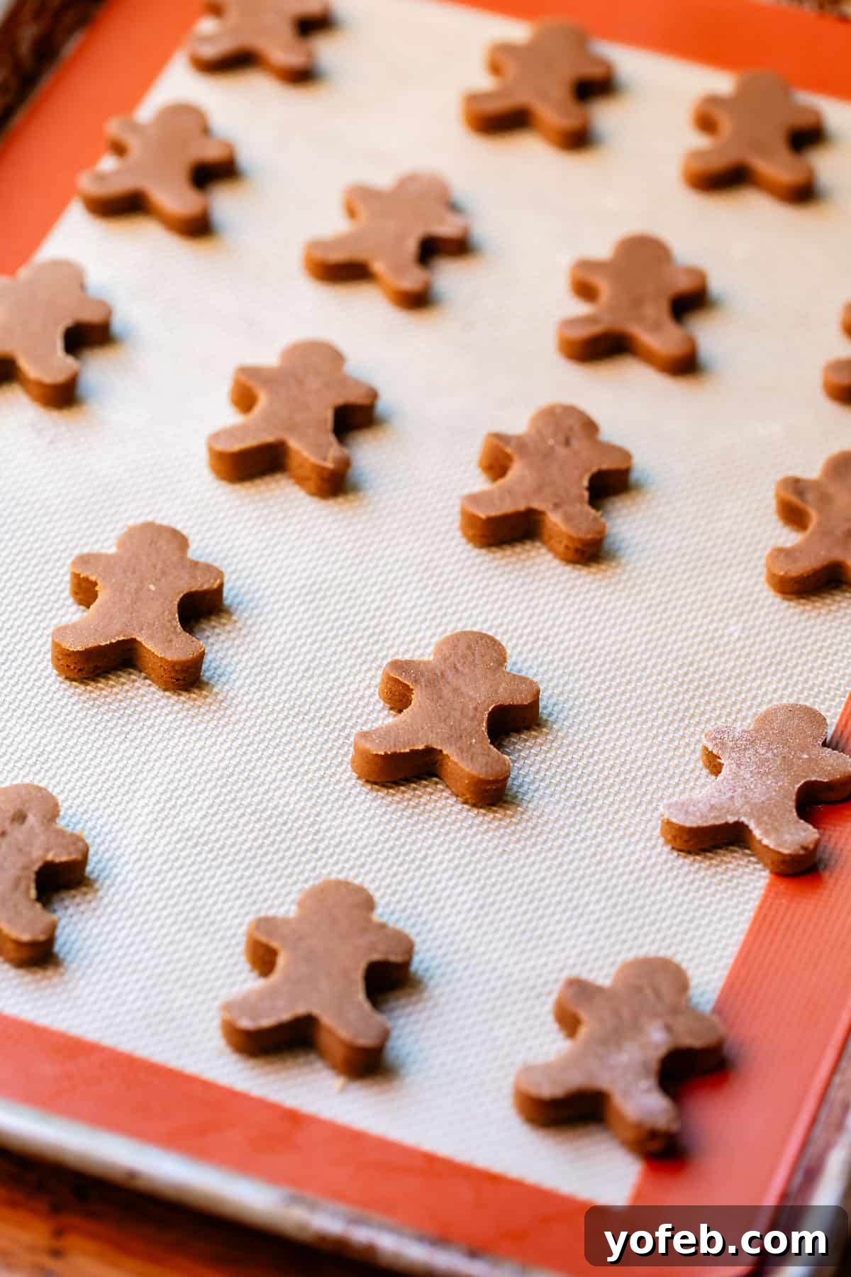 Perfectly Soft Chewy Gingerbread Men That Hold Their Shape 24 A baking sheet covered with a Silpat, filled with numerous tiny cut-out gingerbread men cookies, neatly arranged.