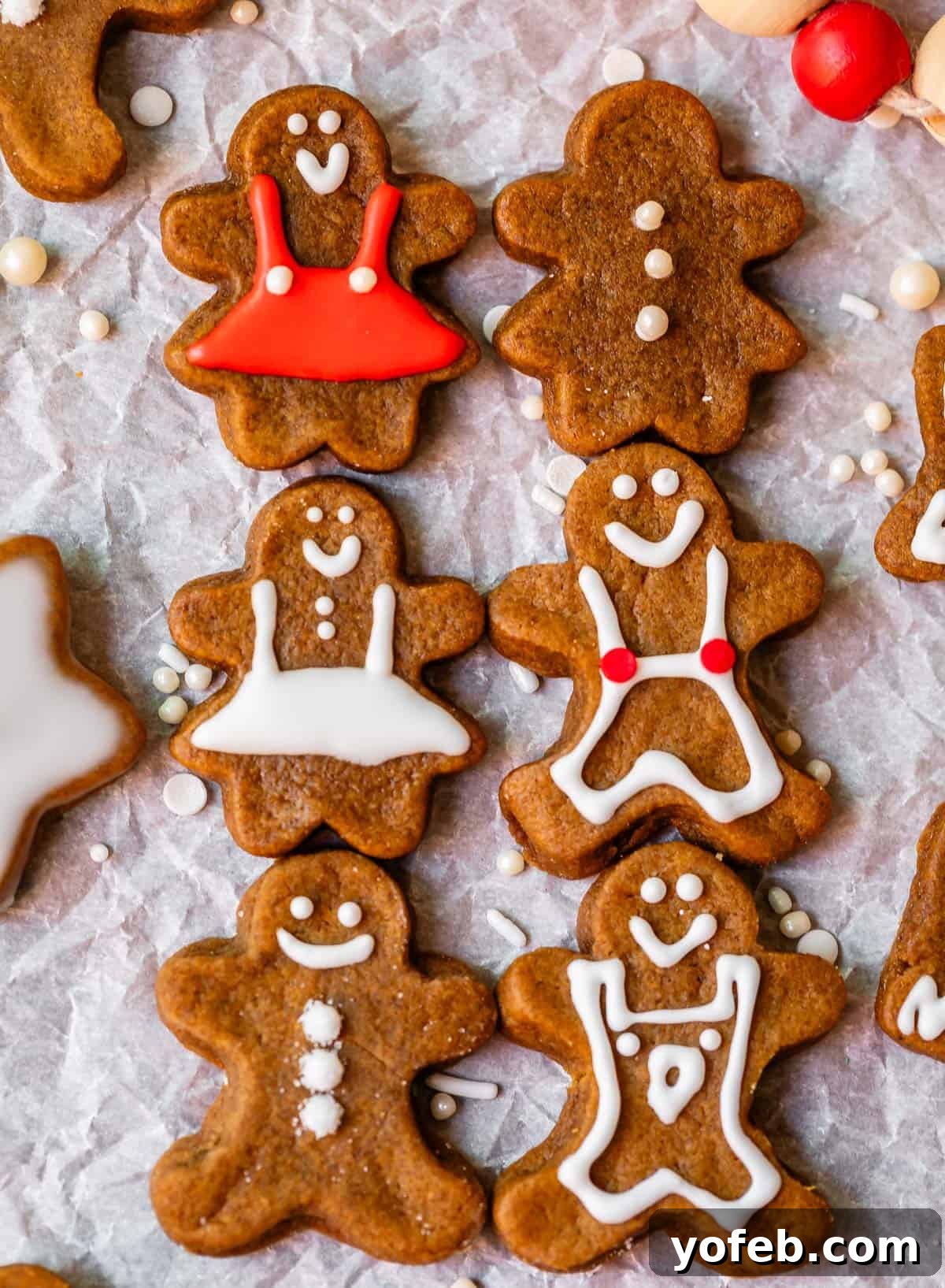 Perfectly Soft Chewy Gingerbread Men That Hold Their Shape 30 Six gingerbread people with white and red icing, neatly lined up on parchment paper, with a festive Christmas tree in the background.