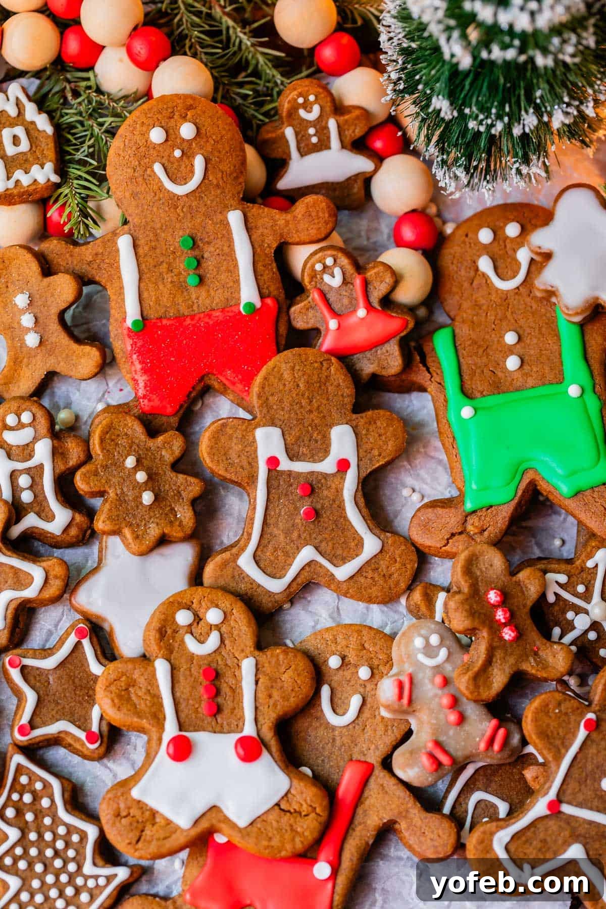 Perfectly Soft Chewy Gingerbread Men That Hold Their Shape 32 Gingerbread cookies adorned with red, white, and green decorations, arranged on parchment paper with a festive Christmas tree in the background.
