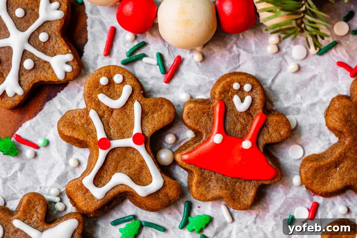 Perfectly Soft Chewy Gingerbread Men That Hold Their Shape 5 Two gingerbread people, one with red and one with white decorations, lying on parchment paper with festive sprinkles around them.