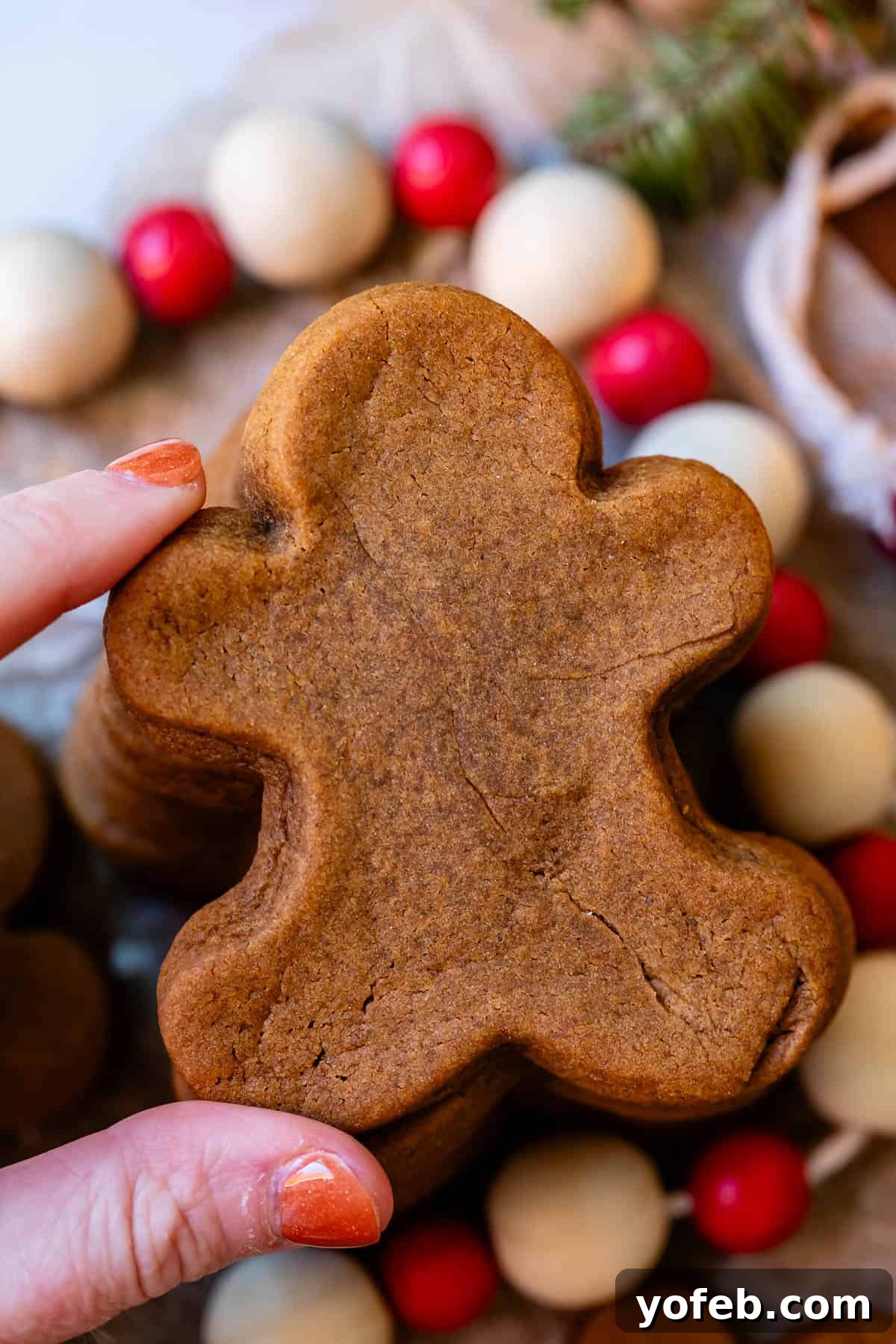 Perfectly Soft Chewy Gingerbread Men That Hold Their Shape 8 A perfectly soft gingerbread man cookie at the top of a stack, being picked up by a hand from the left, highlighting its desirable texture.