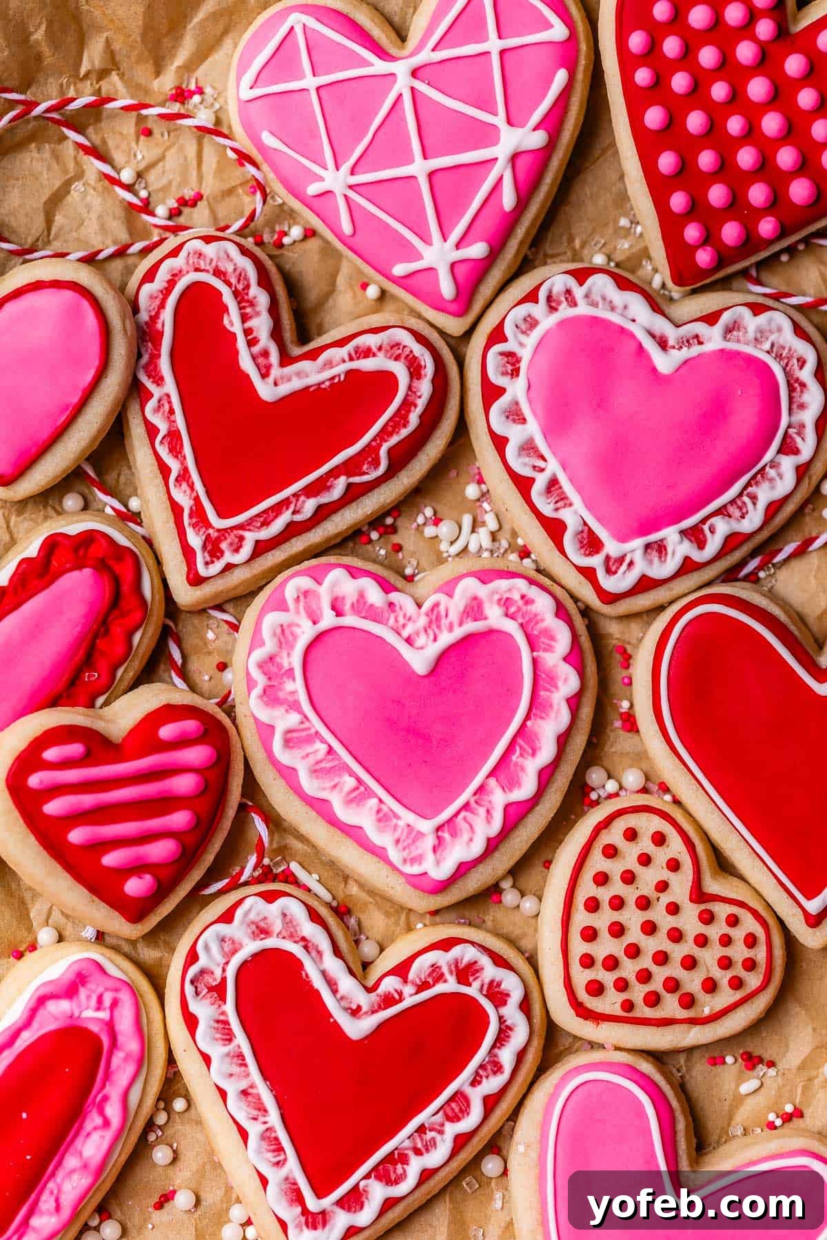 Beginner's Guide to Perfect Royal Icing 3 overhead shot of red and pink heart sugar cookies on parchment paper, frosted with royal icing.