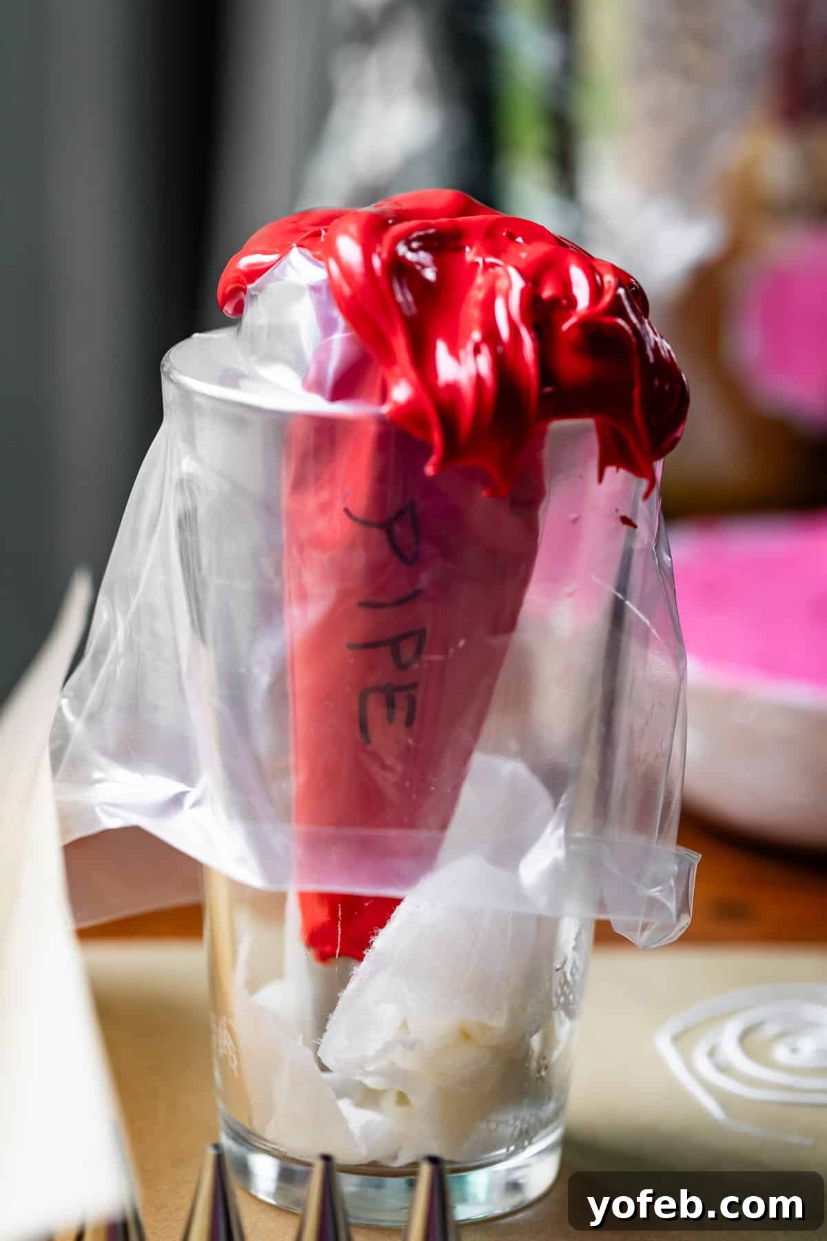 Beginner's Guide to Perfect Royal Icing 25 decorating bag with word "pipe" on it filled with red royal icing in a tall cup.