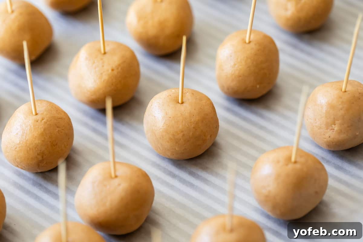 Irresistible Buckeye Ball Recipe 14 Peanut butter dough balls lined on a baking sheet with toothpicks inserted, ready to freeze.