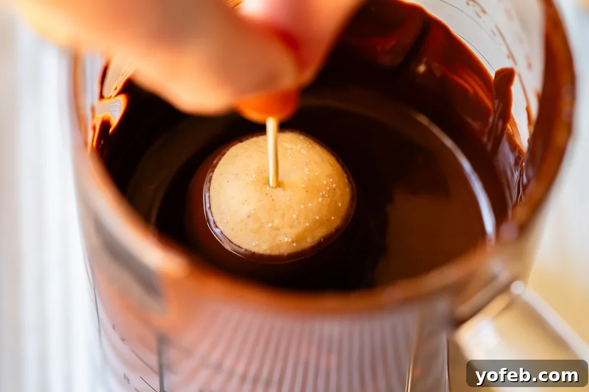 Irresistible Buckeye Ball Recipe 18 Close-up of fingers holding a toothpick in a peanut butter dough ball being dipped into chocolate.