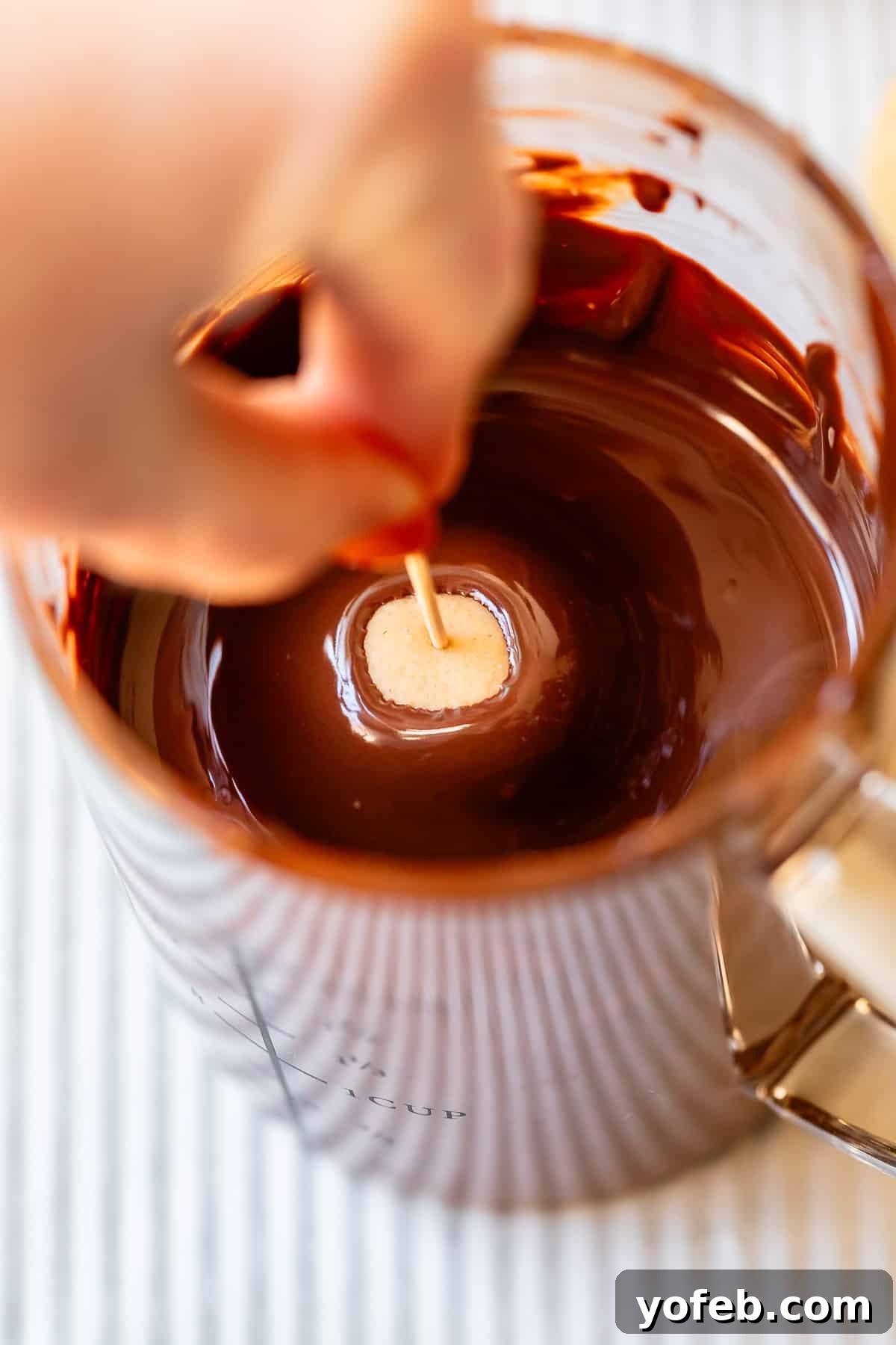 Irresistible Buckeye Ball Recipe 19 A hand dipping a peanut butter dough ball into melted chocolate to make buckeyes.