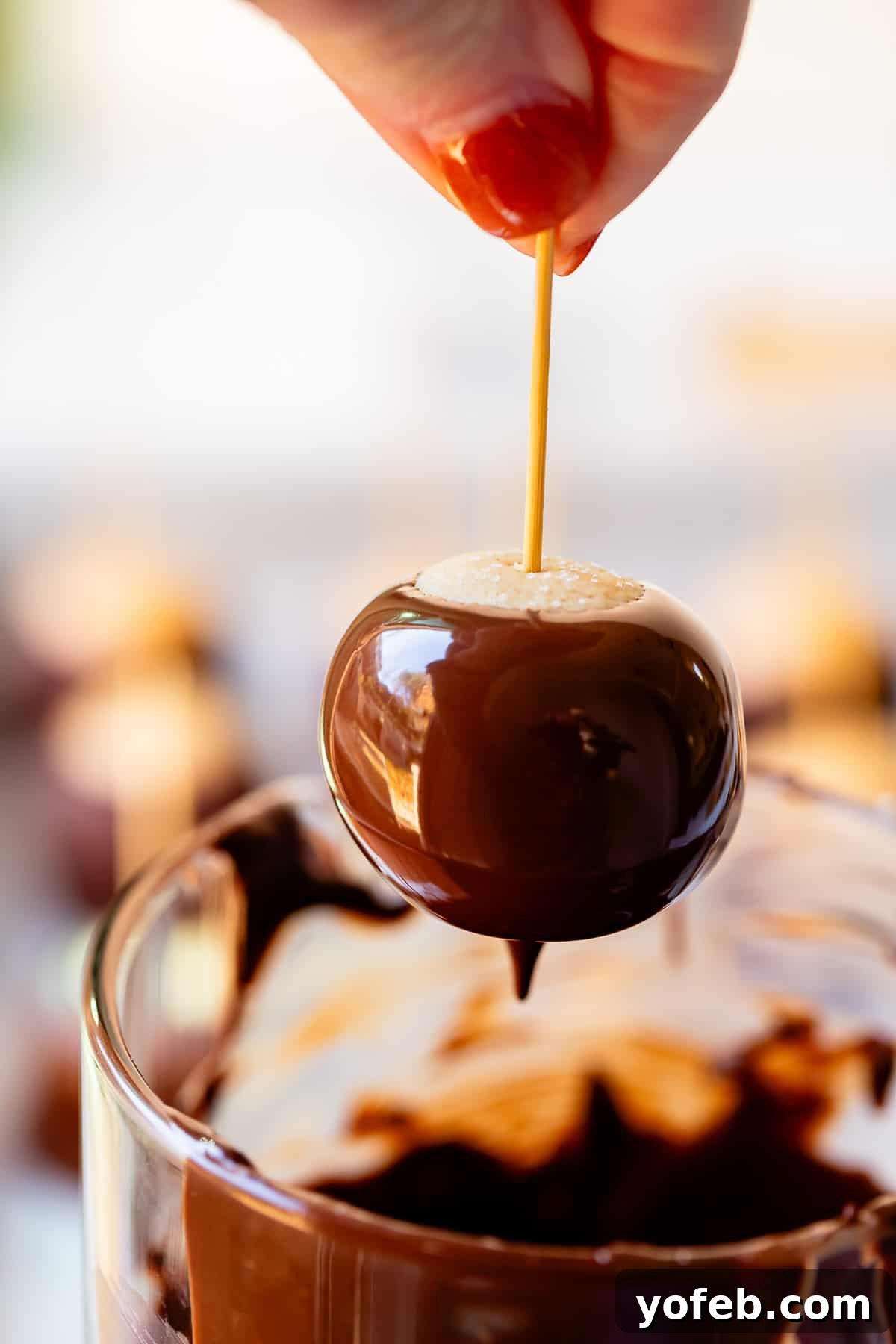 Irresistible Buckeye Ball Recipe 20 Hand holding a freshly dipped buckeye by the toothpick over the dipping bowl to drip off excess chocolate.