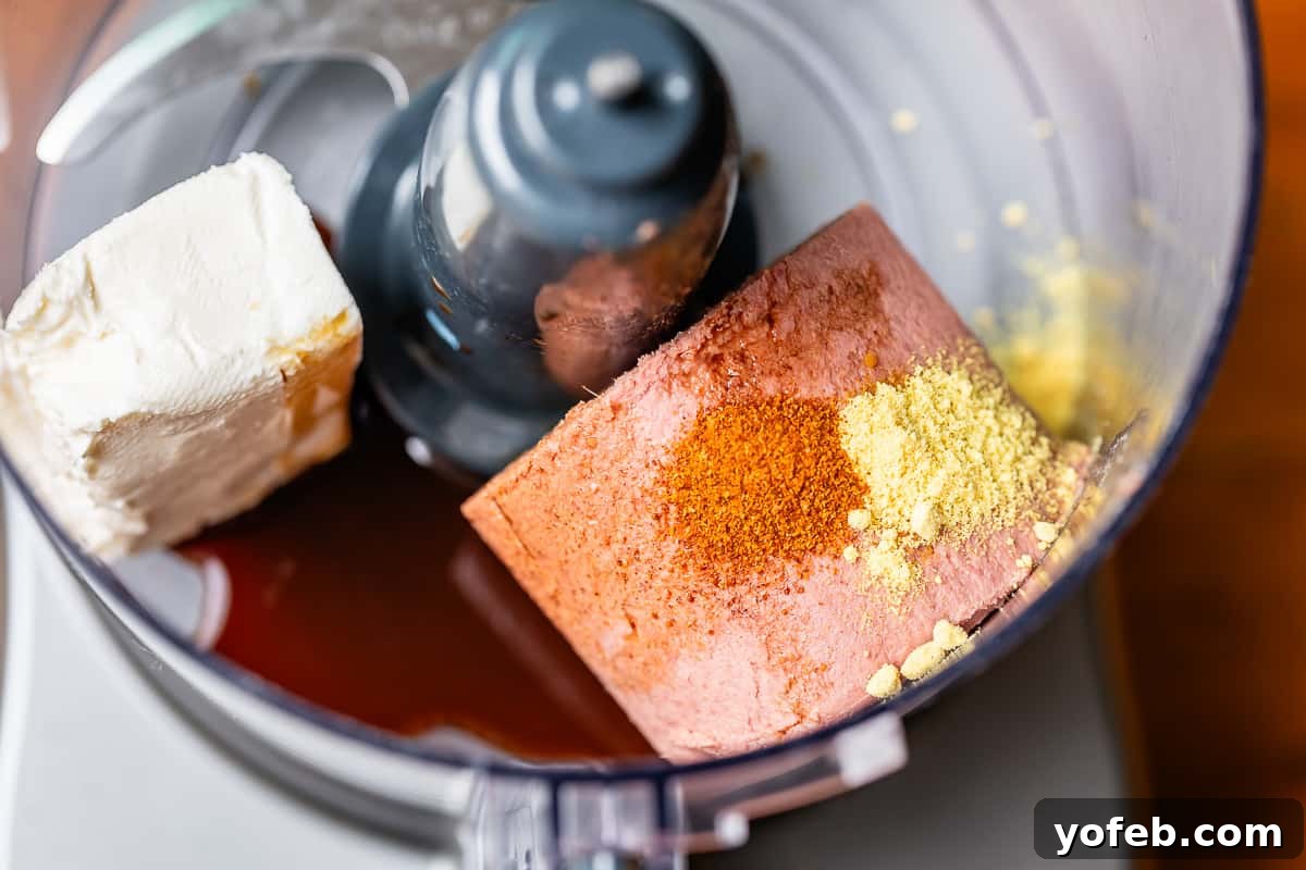 A food processor filled with Braunschweiger, cream cheese, Worcestershire sauce, dry mustard, and cayenne pepper, captured mid-blend as the ingredients transform into a smooth pâté.