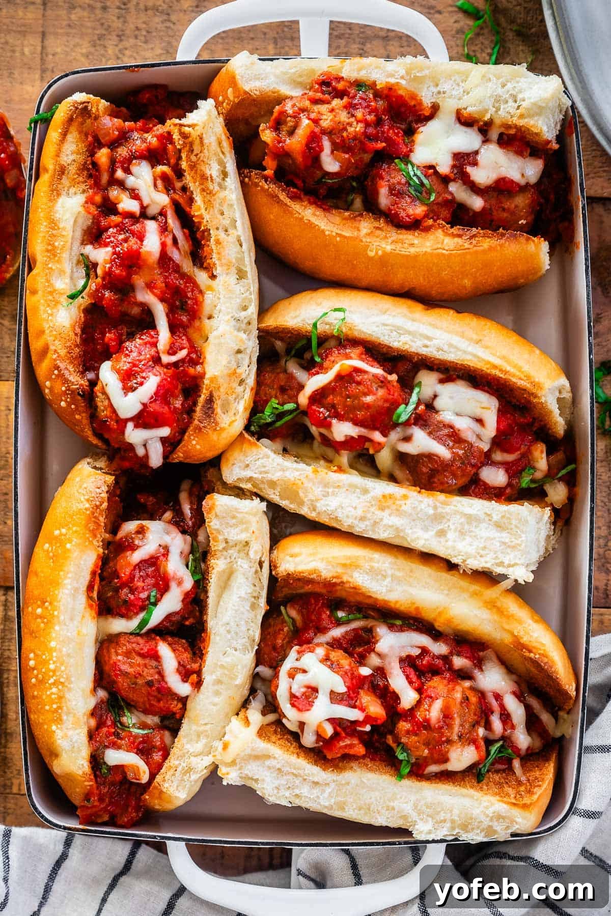 Laura's Ultimate Meatball Sub 14 A baking dish filled with several toasted hoagie rolls, generously stuffed with tender meatballs and rich sauce, all blanketed under a layer of golden, melted cheese, ready for serving.
