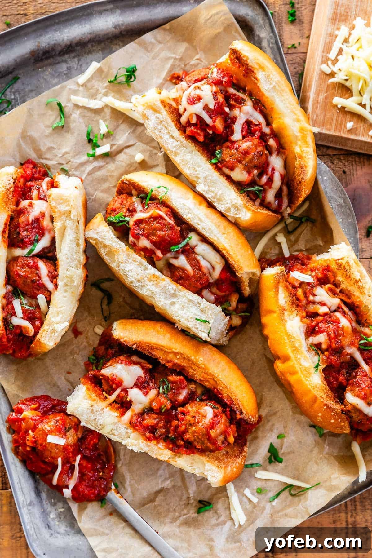 Laura's Ultimate Meatball Sub 16 A metal serving tray showcasing several fully assembled, mouth-watering meatball subs on parchment paper, each with toasted buns, generous meatballs and sauce, and perfectly melted cheese, ready to be served.
