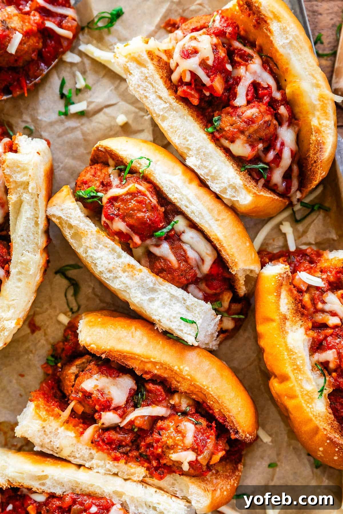 Laura's Ultimate Meatball Sub 3 Several piping hot meatball sandwiches with melted cheese, glistening with sauce, arranged neatly on parchment paper, ready to be served.
