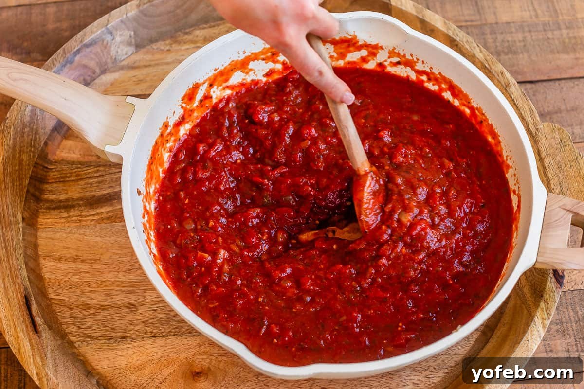 Laura's Ultimate Meatball Sub 8 A generous can of crushed tomatoes being poured into the large skillet, joining the sautéed onions, spices, and tomato paste to form the base of the rich marinara sauce.
