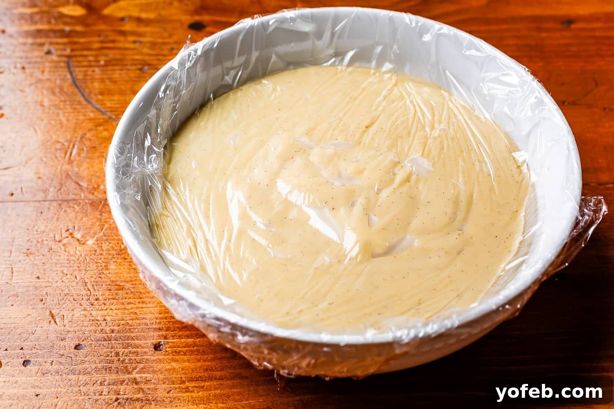 Luscious Caramel Swirled Coconut Cream Pie 11 plastic wrap pressed directly up against coconut custard in a ceramic bowl.